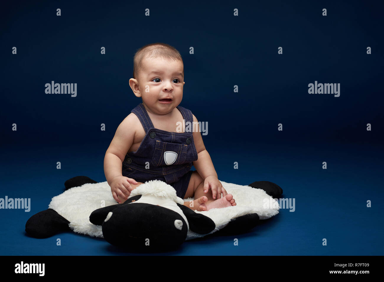 Scared baby boy sit on pillow in blue studio background Stock Photo
