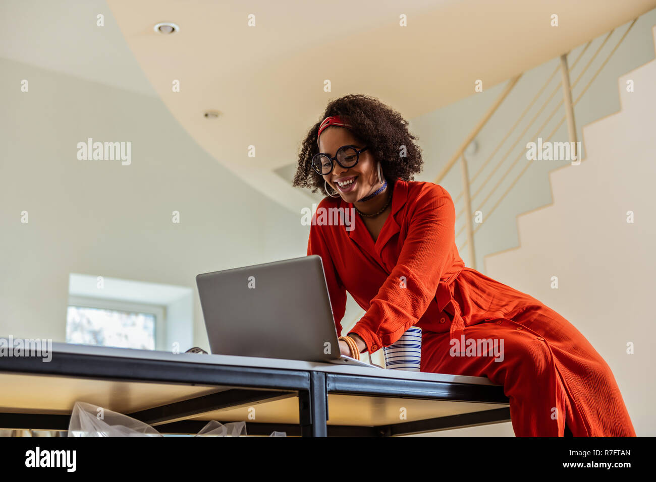 Widely smiling attractive lady sitting on table with laptop Stock Photo