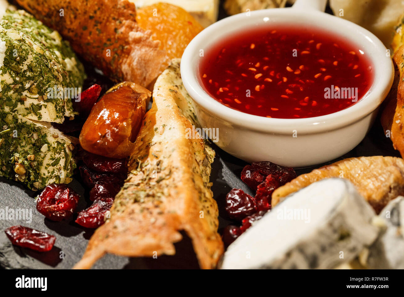 Bowl with cranberry sauce stands between pieces of cheese on black plate Stock Photo