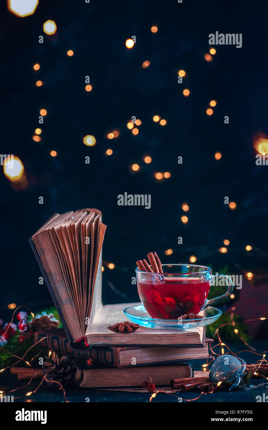 Red berry tea on a stack of books with fairy lights. Christmas drink on a dark background with copy space Stock Photo