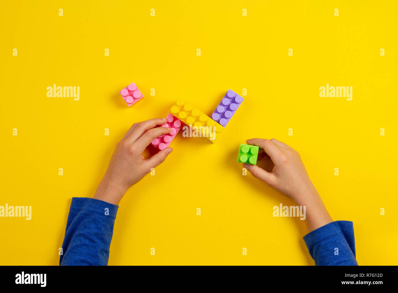 Kid hands playing with colorful plastic bricks on yellow background ...