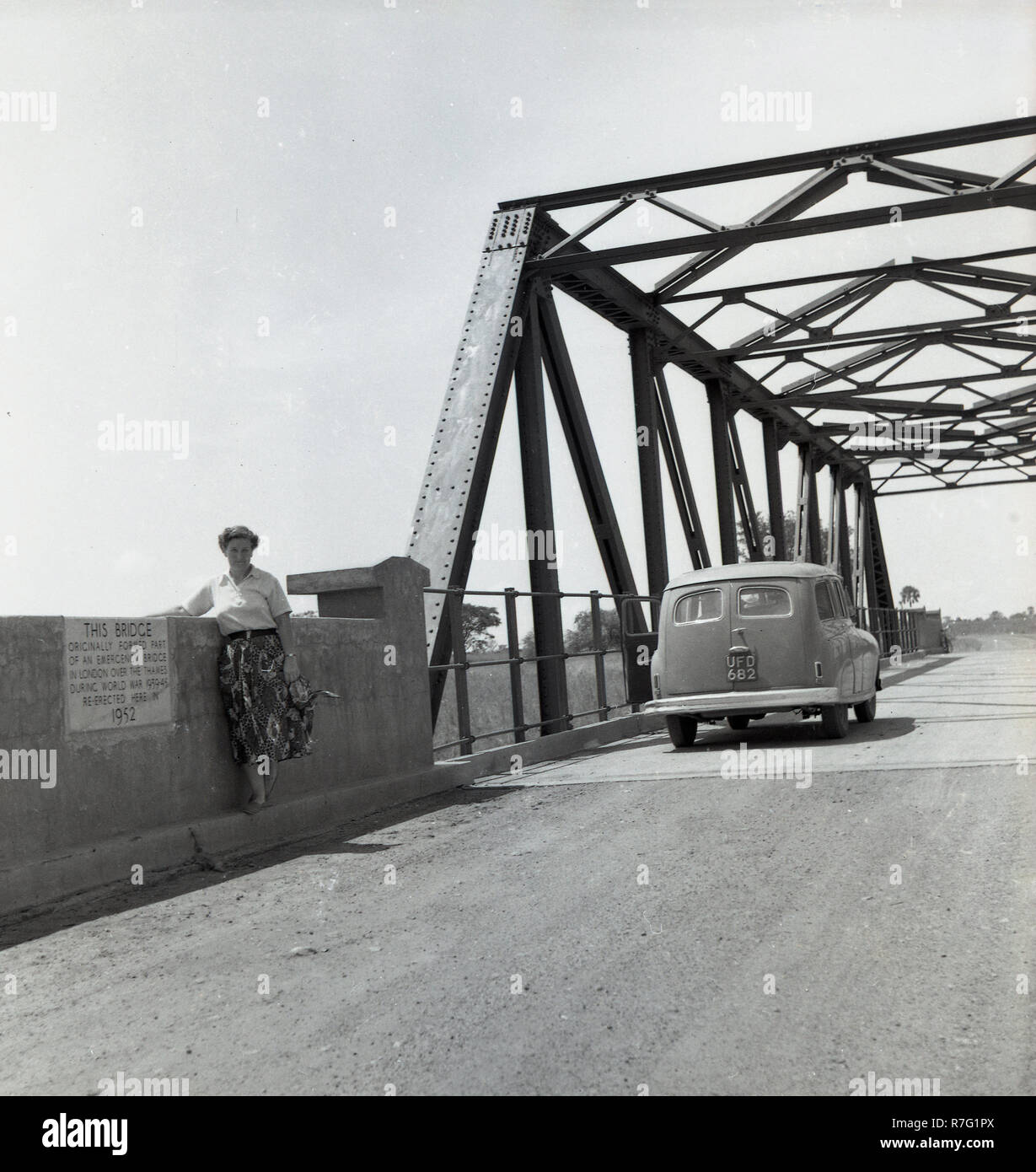 1950s, Africa, Uganda, a lady traveller, standing by a wall, with a plaque on, stating that this was a re-erected emergency steel bridge which had built over the Thames during WW2 between 1939-1945. Stock Photo