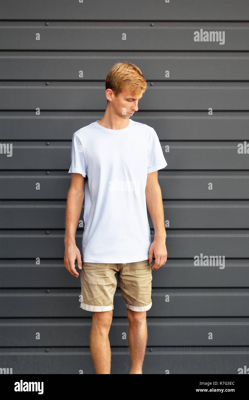 Urban mockup of clothes. Young man standing near the gray metal profiled  wall in a white T-shirt and brown shorts. Template can use for you desig  Stock Photo - Alamy