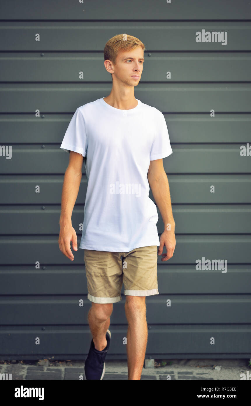 Urban template of clothes. Young slim man coming from the gray metal  profiled wall in a white T-shirt and brown shorts. Mockup can use for you s  Stock Photo - Alamy