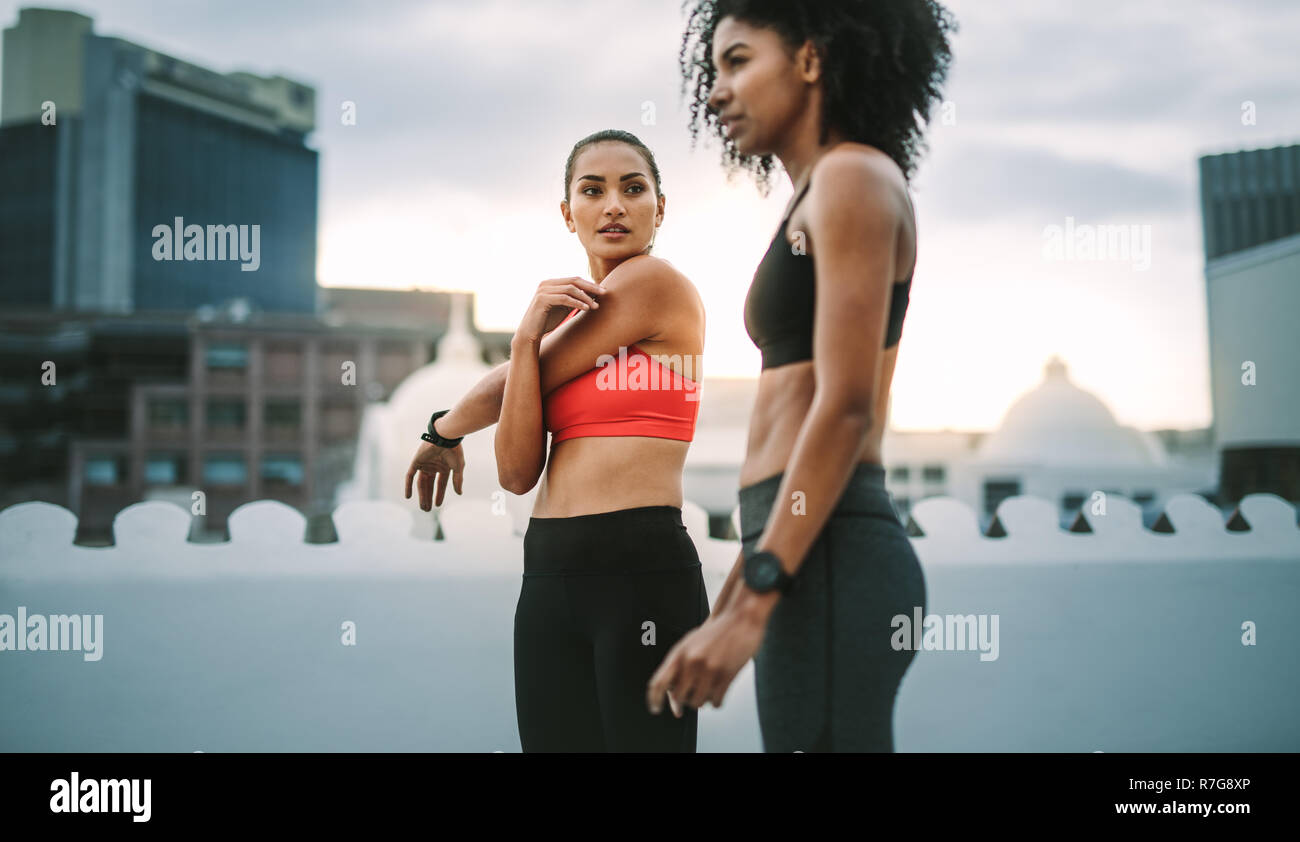 Two female athletes doing workout standing on rooftop. Women in fitness clothes doing fitness training on terrace with high rise buildings in the back Stock Photo
