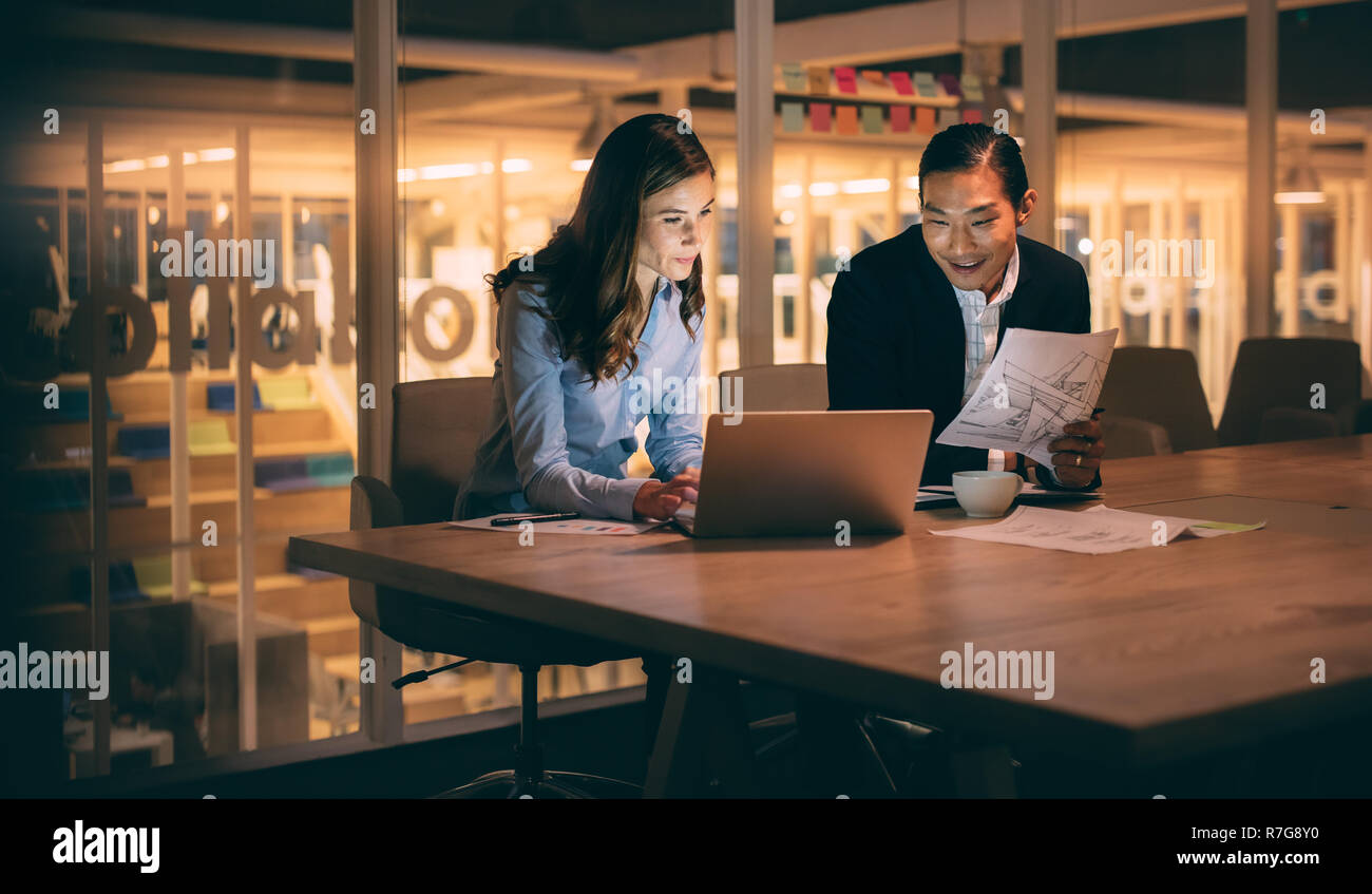 Businessman and woman discussing business work sitting late in office. Woman entrepreneur working on laptop sitting with her business partner. Stock Photo