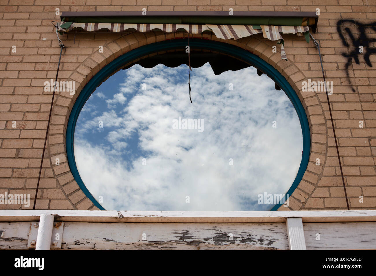 Circular window reflecting clouds perfectly on abandoned building. Stock Photo