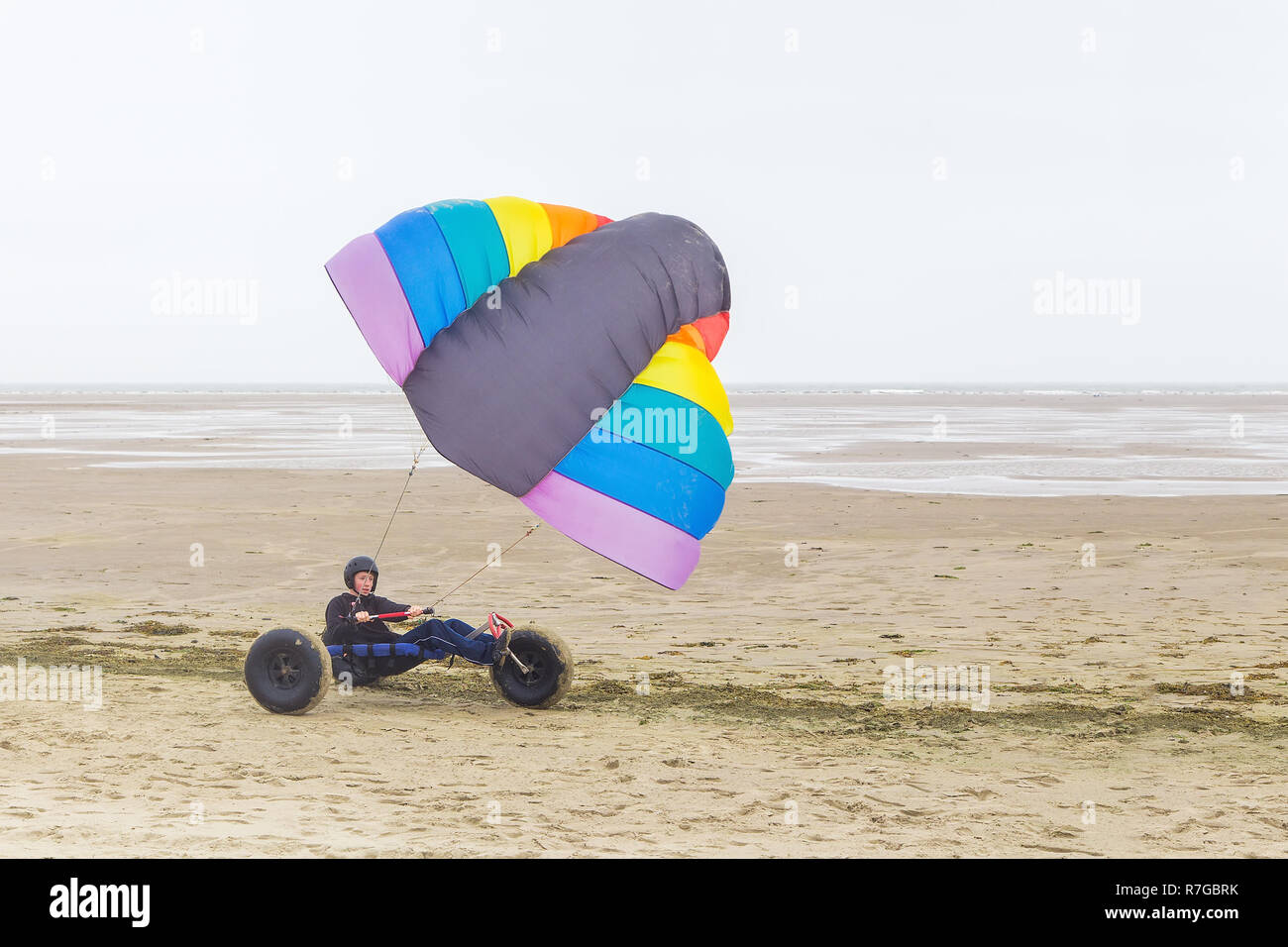 Caucasian male teen drivesg kite buggy with kite flyer on beach with sea Stock Photo