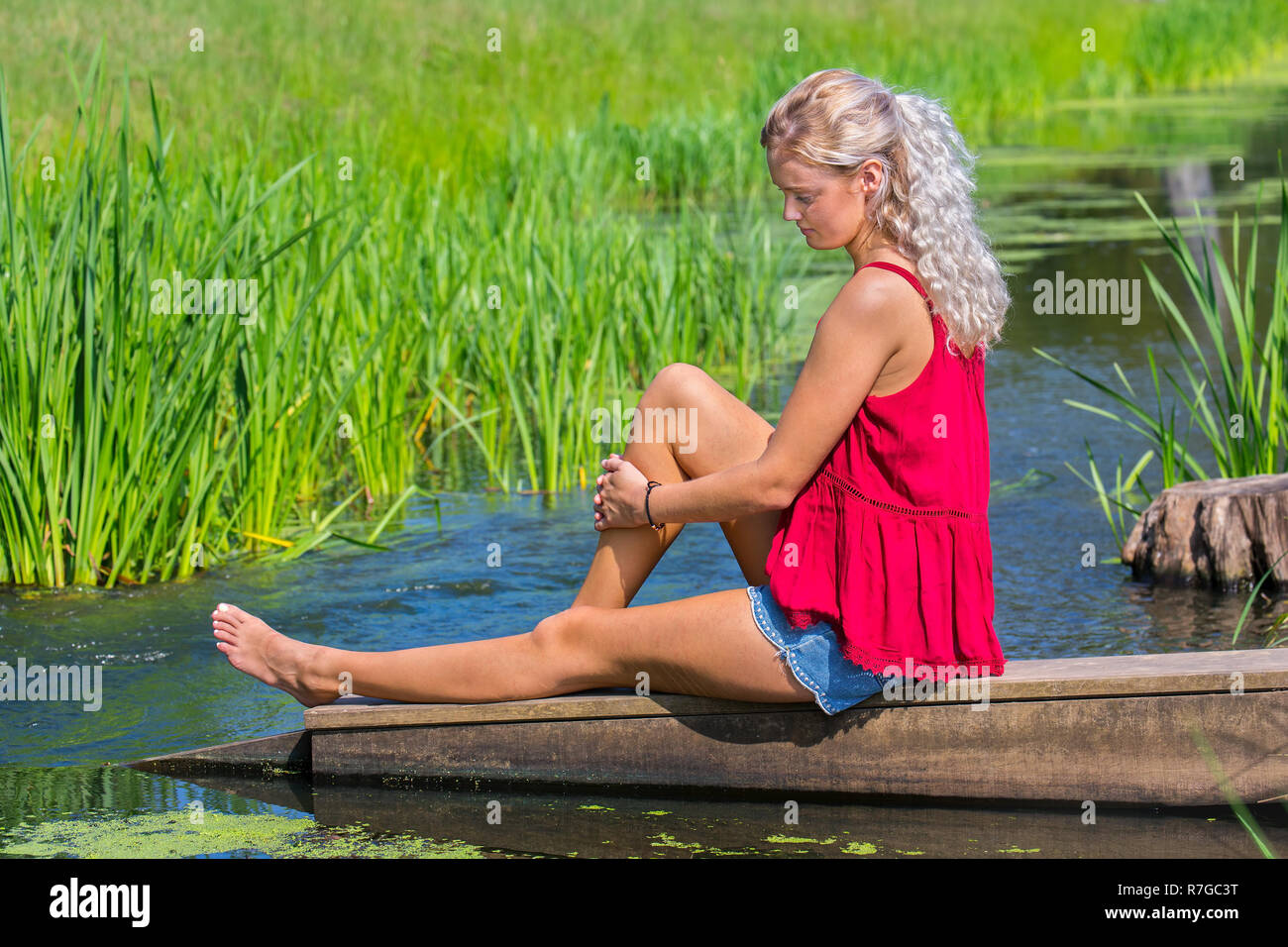 Young blond caucasian woman musing at water in nature Stock Photo