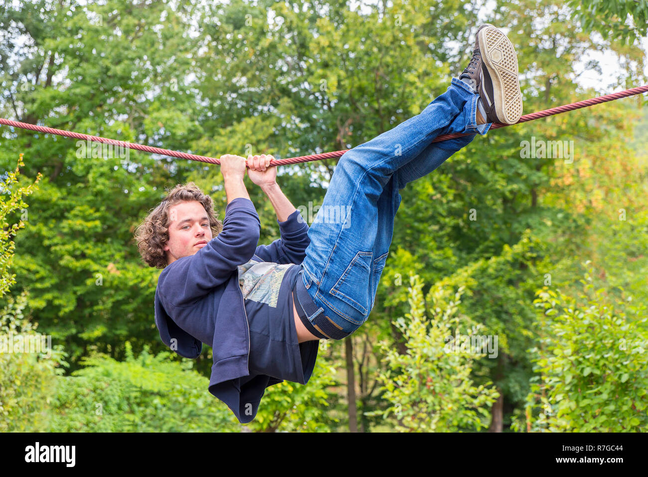 Young caucasian man hanging at climbing rope outdoors Stock Photo