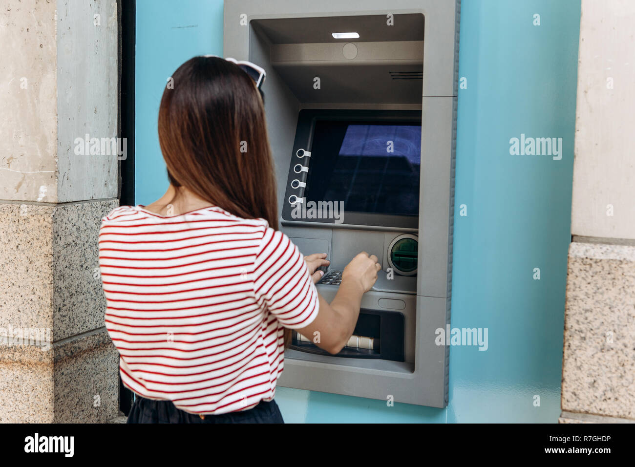 A young woman takes money from an ATM. Finance, credit card, withdrawal of money. Life style. Grabs a card from the ATM. Stock Photo