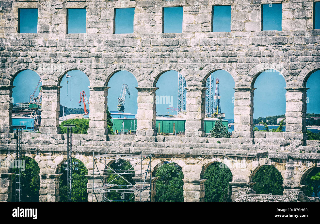 Pula Arena and cranes in a cargo port, Istria, Croatia. Travel destination. Ancient architecture. Analog photo filter with scratches. Stock Photo