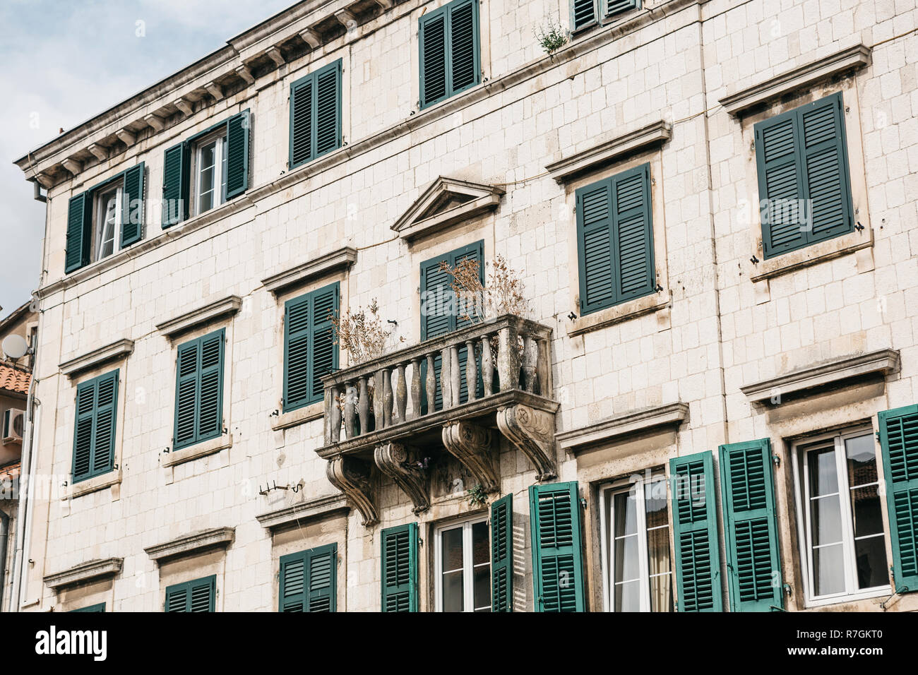 The facade of an ordinary old building with windows and a balcony in Montenegro. Some windows are closed by shutters. Traditional housing. Stock Photo