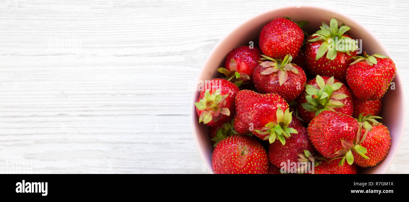 Fresh organic strawberries in a pink ceramic bowl on white wooden ...