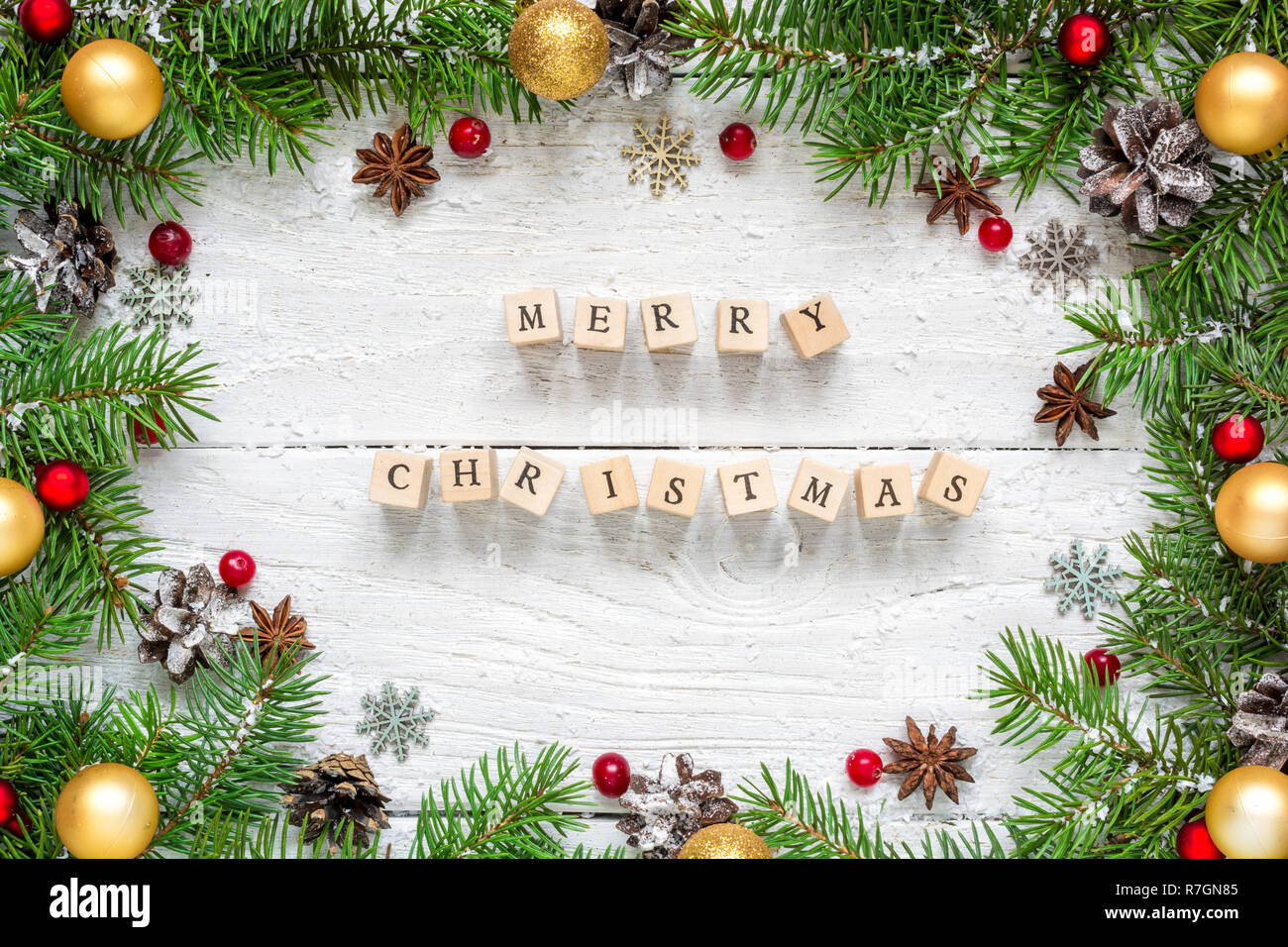 merry christmas inscription in frame made of fir branches, festive decorations and pine cones on white wooden table. Christmas background. Flat lay. t Stock Photo