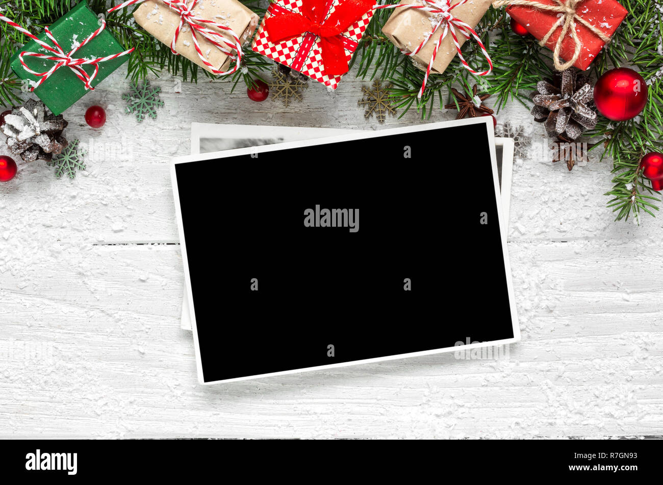 christmas blank photo frame with fir tree branches, decorations and gift boxes over white wooden background. mock up. flat lay. top view Stock Photo