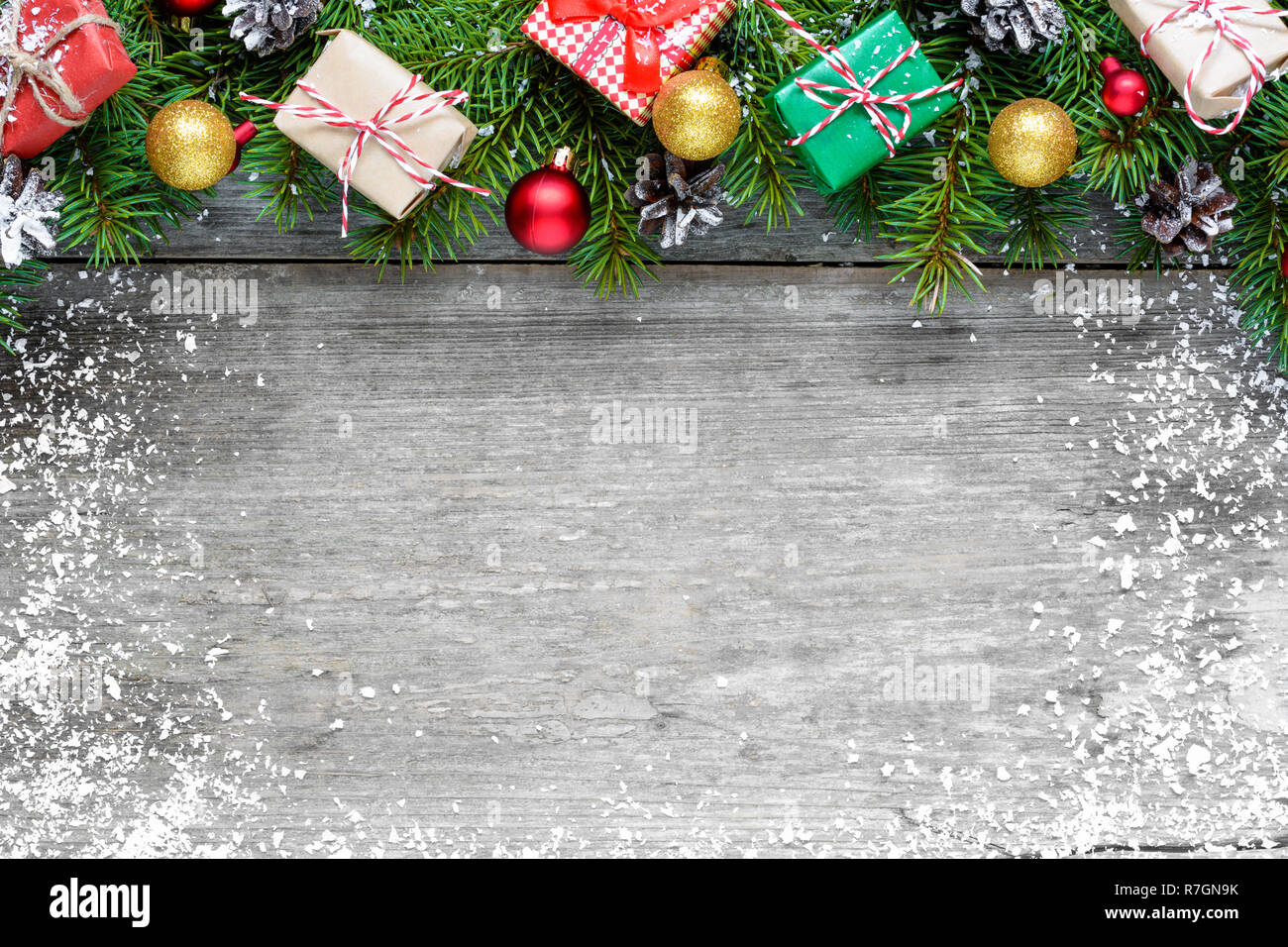 Christmas background with fir branches, decorations, gift boxes and pine cones on rustic wooden table covered with snow. Christmas background. Flat la Stock Photo