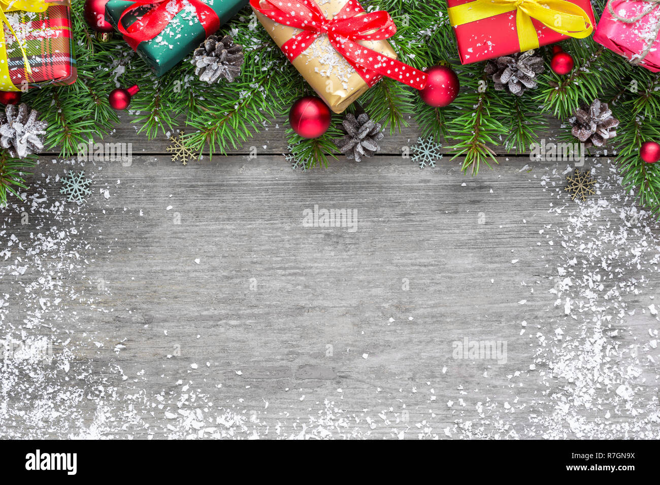 Christmas background with fir branches, red balls, gift boxes and pine cones on rustic wooden table covered with snow. Flat lay. top view with copy sp Stock Photo
