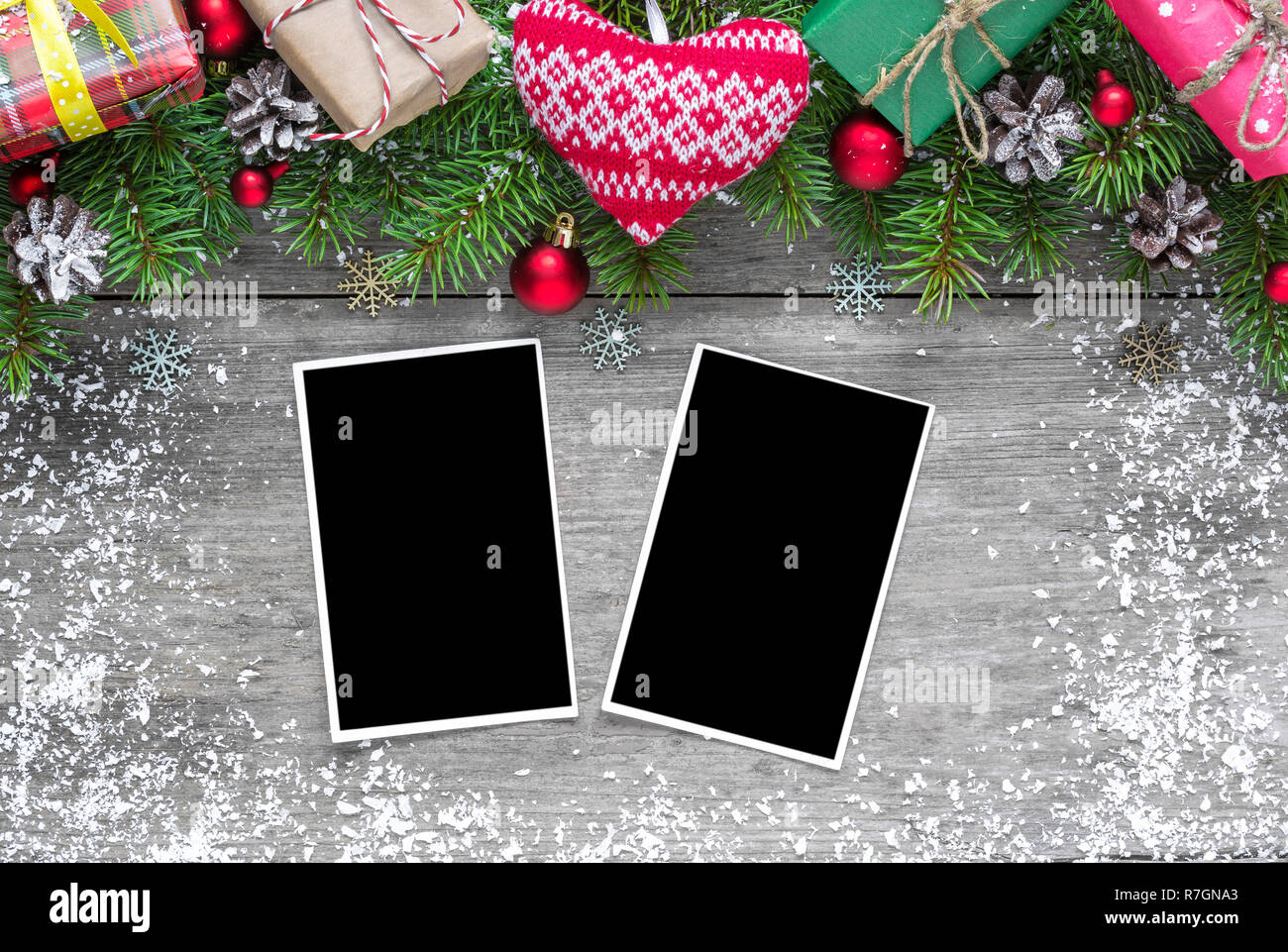 christmas blank photo frames with fir tree branches, decorations, gift boxes and knitted heart over rustic wooden background. mock up. flat lay. top v Stock Photo