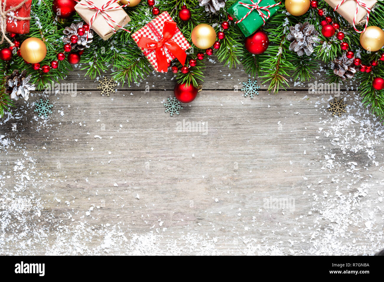 Christmas background with fir branches, red and golden balls, gift boxes and pine cones on rustic wooden table covered with snow. Flat lay. top view w Stock Photo