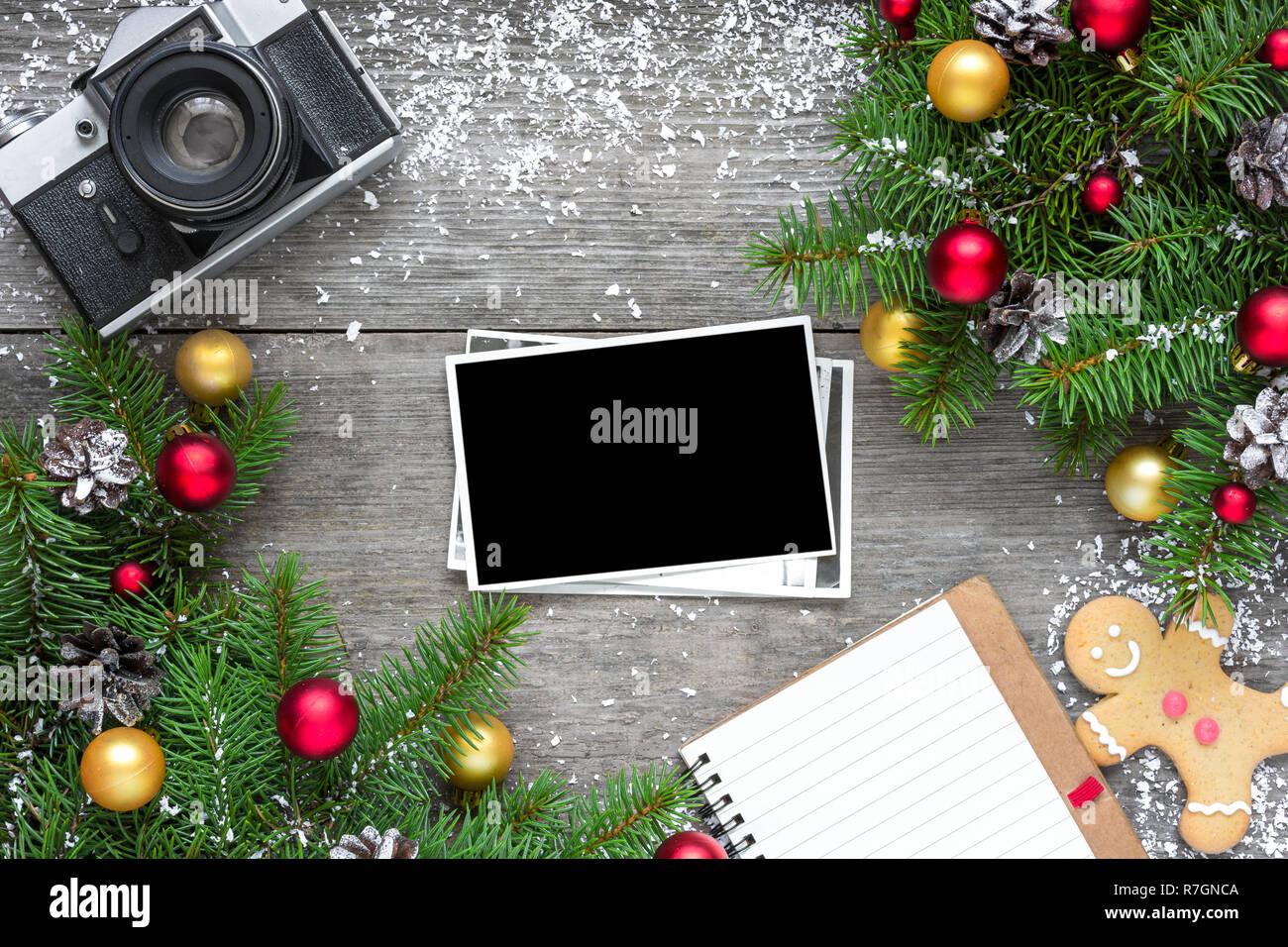 retro camera and christmas blank photo frame with fir tree branches, decorations and lined notebook over rustic wooden background. mock up. flat lay.  Stock Photo