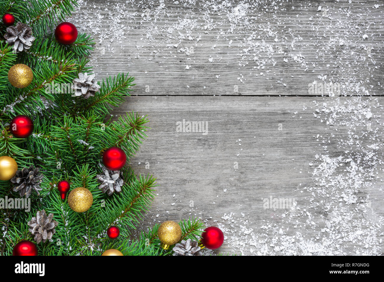 Christmas background with fir tree branches, red and golden decorations and pine cones on rustic wooden table covered with snow. Flat lay. top view wi Stock Photo