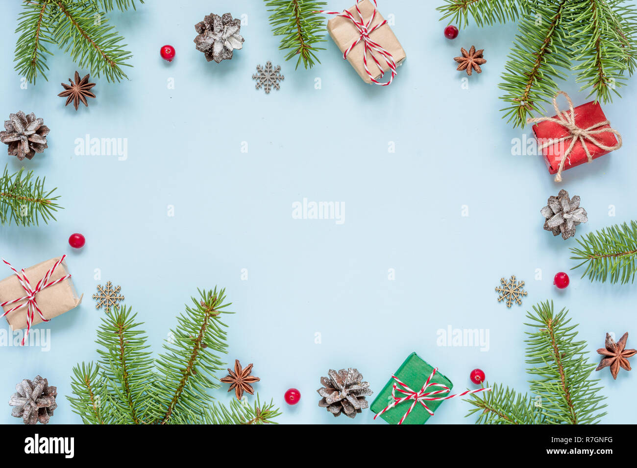 Christmas composition made of frame of fir branches, red berries, gift boxes and pine cones on blue background. Christmas background. Flat lay. top vi Stock Photo