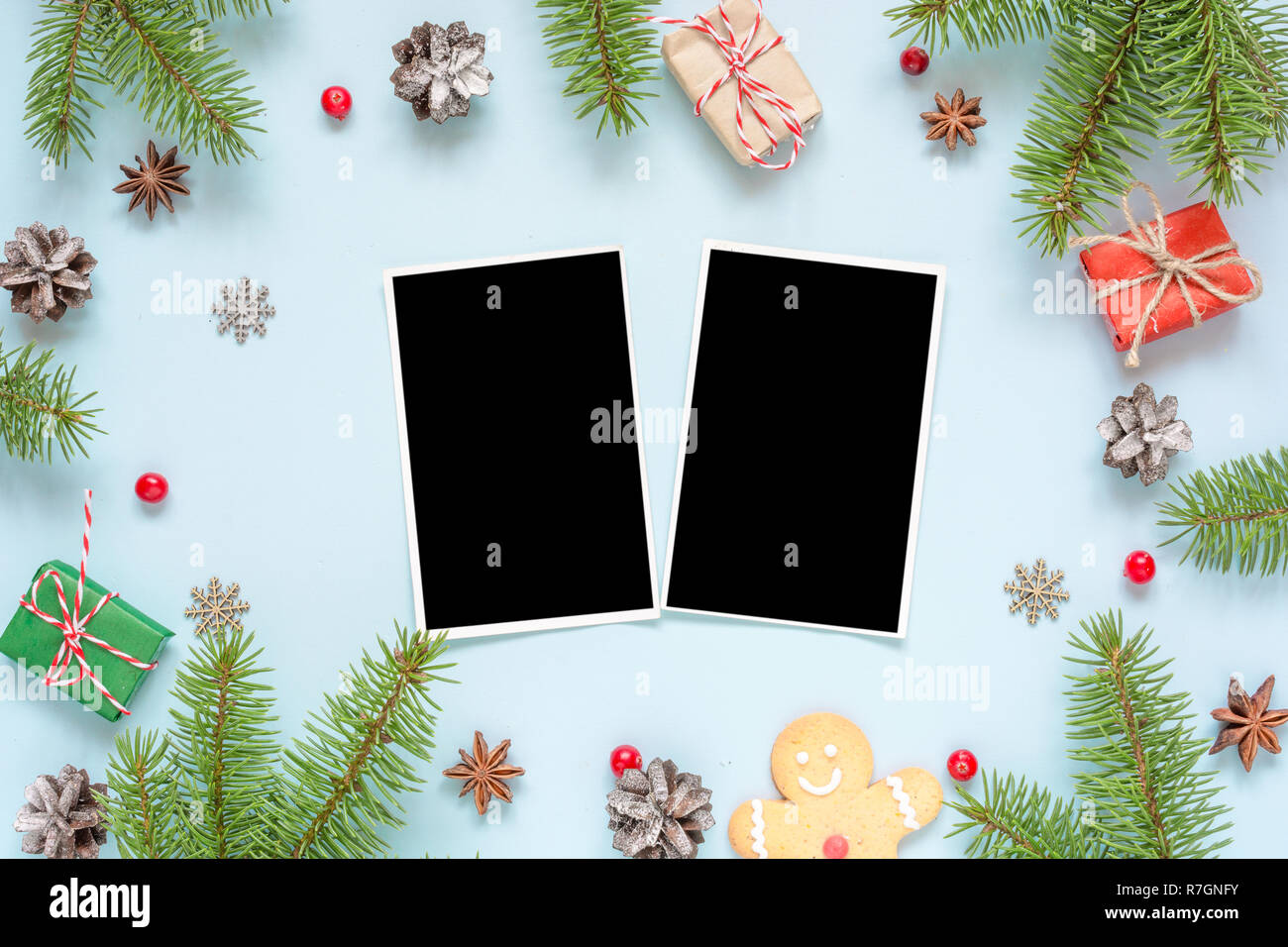 christmas blank photo cards in frame made of fir tree branches, decorations and gift boxes over blue background. mock up. flat lay. top view Stock Photo