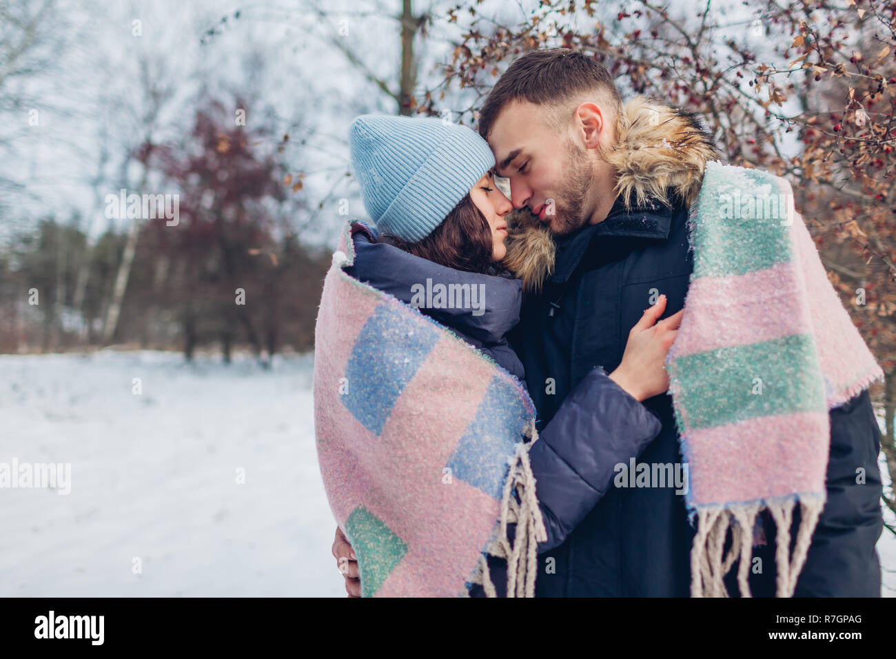 Beautiful loving couple walking and hugging in winter forest. Happy people warming covered with blanket. Stock Photo