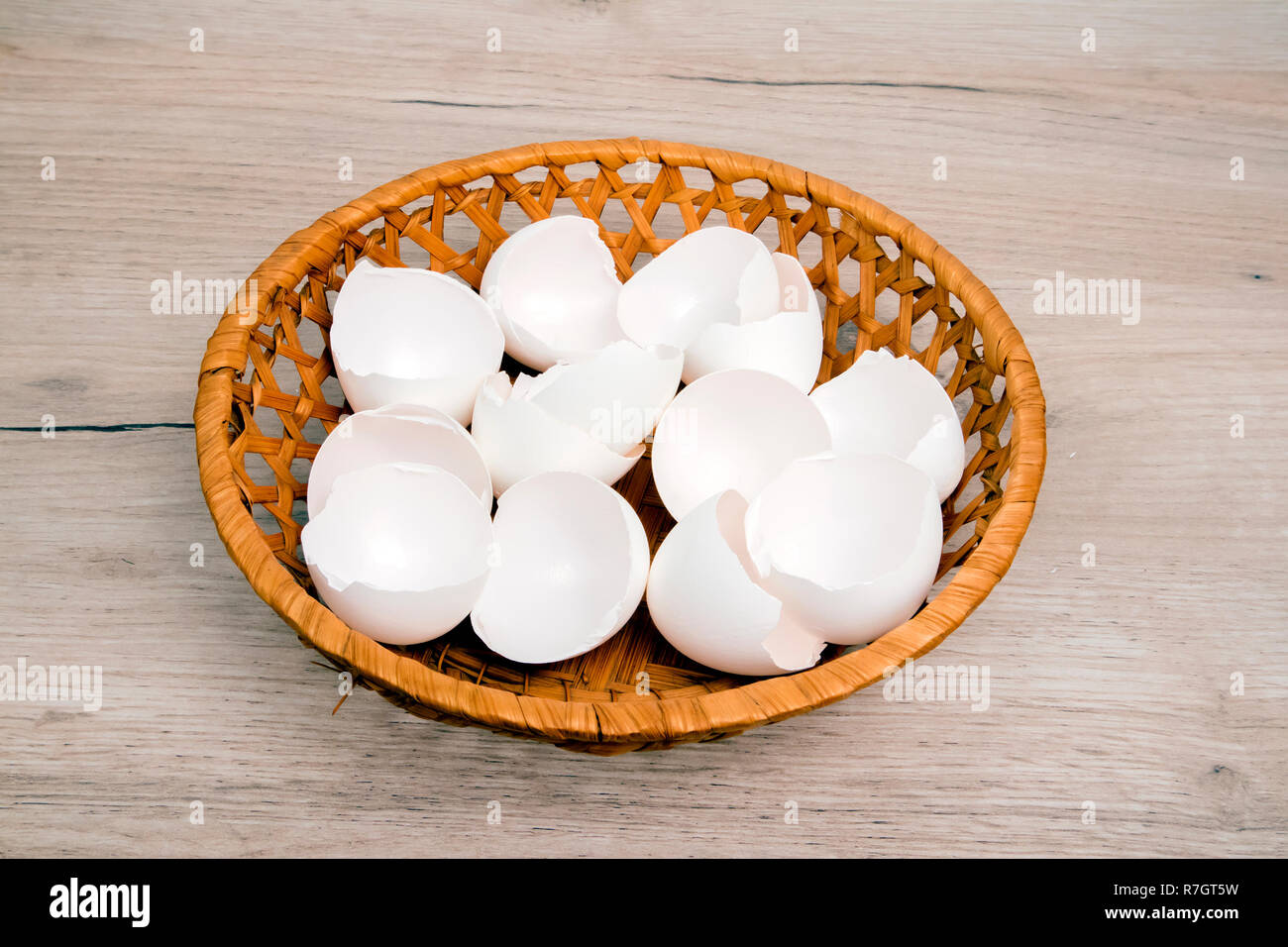 A pile of empty  white egg shells in wicker basket placed on wooden board Stock Photo