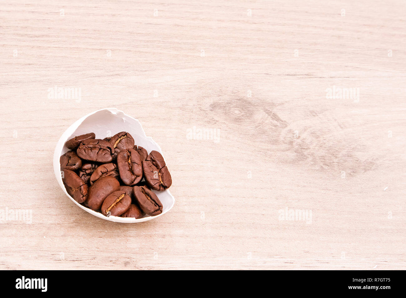 A half of white egg shell full of roasted coffee beans placed on a wooden surface Stock Photo