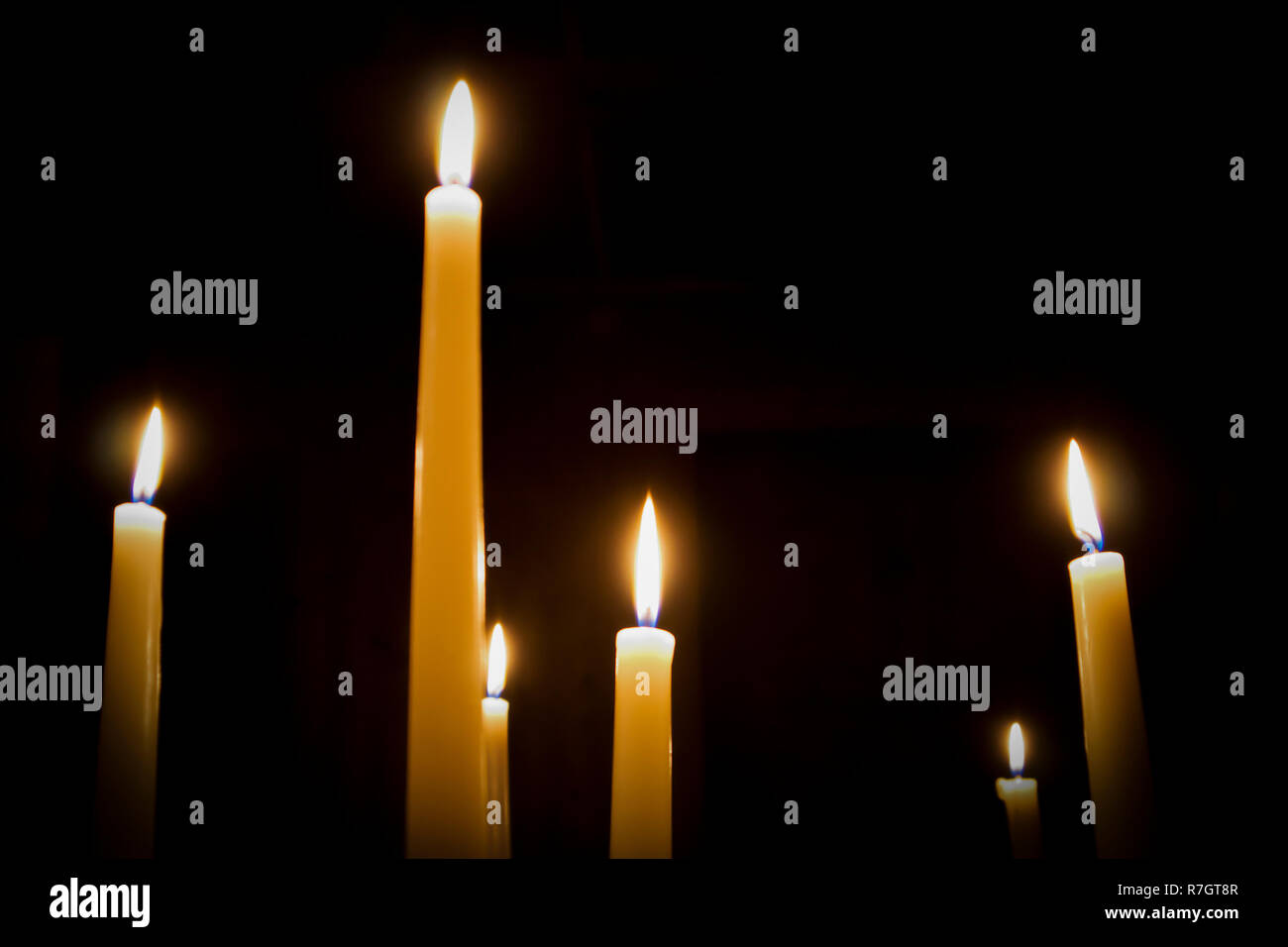 A number of burning melted candles with blurred forks of flame against dark background Stock Photo
