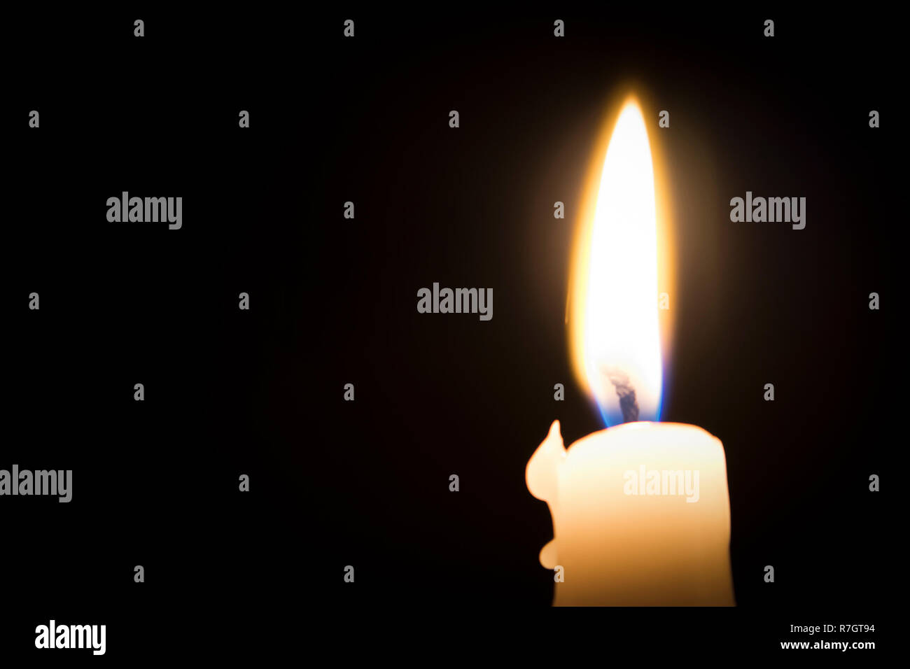 Single burning melted candle with blurred fork of flame against dark ...