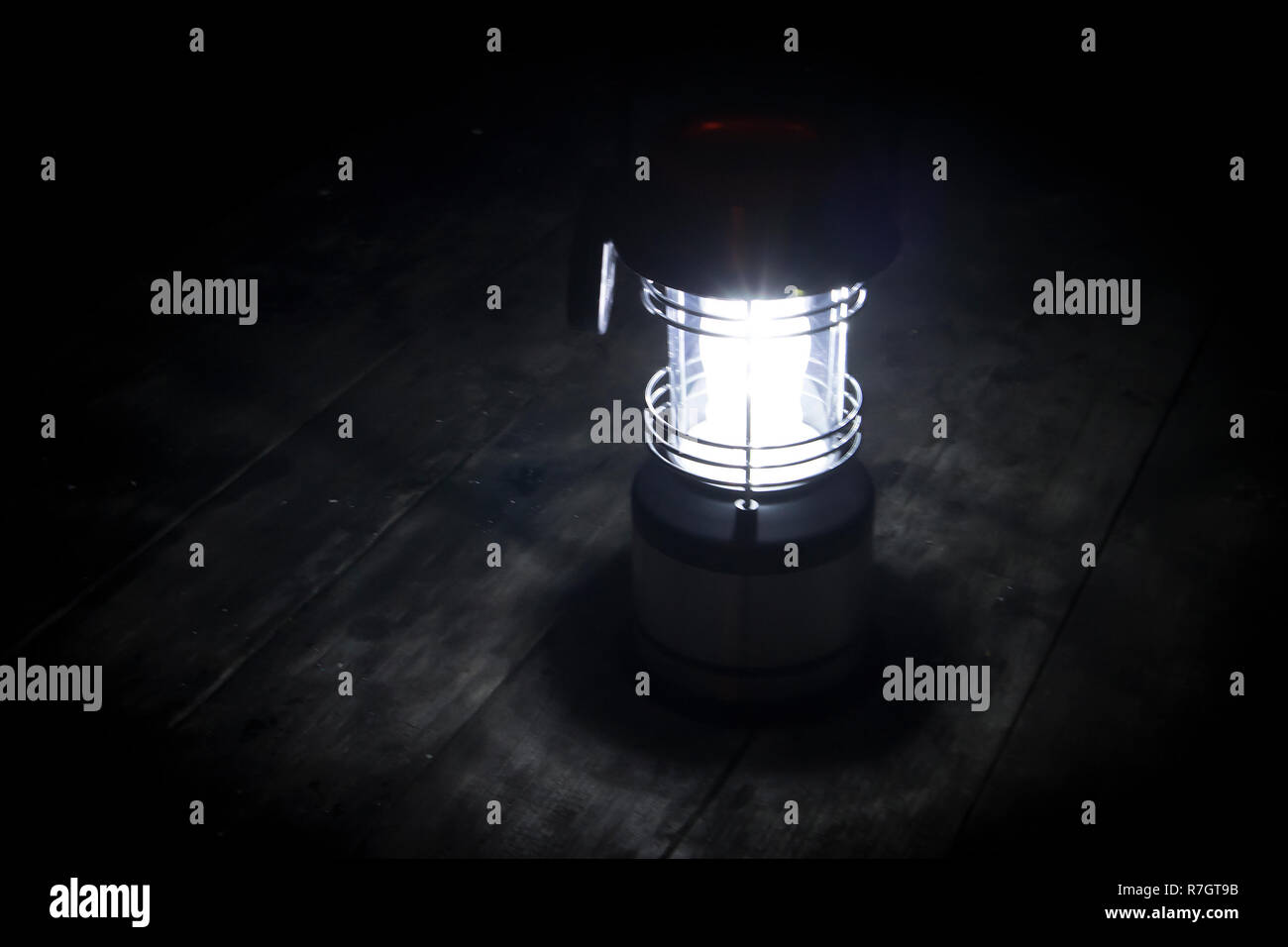 Grunge photo of lighted wireless lantern standing in the night on a wooden surface Stock Photo