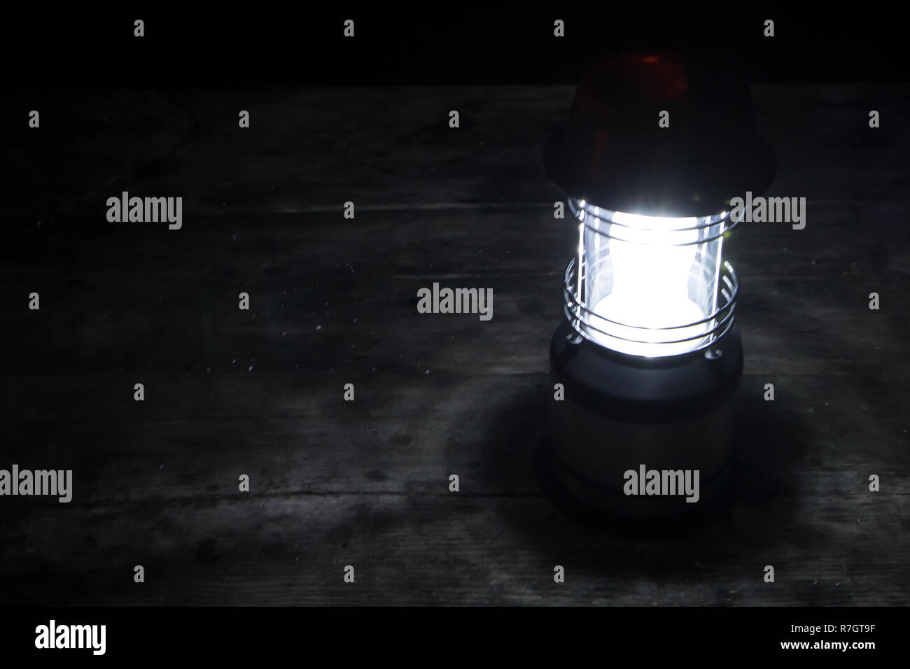 Grunge photo of lighted wireless lantern standing in the night on a wooden surface Stock Photo