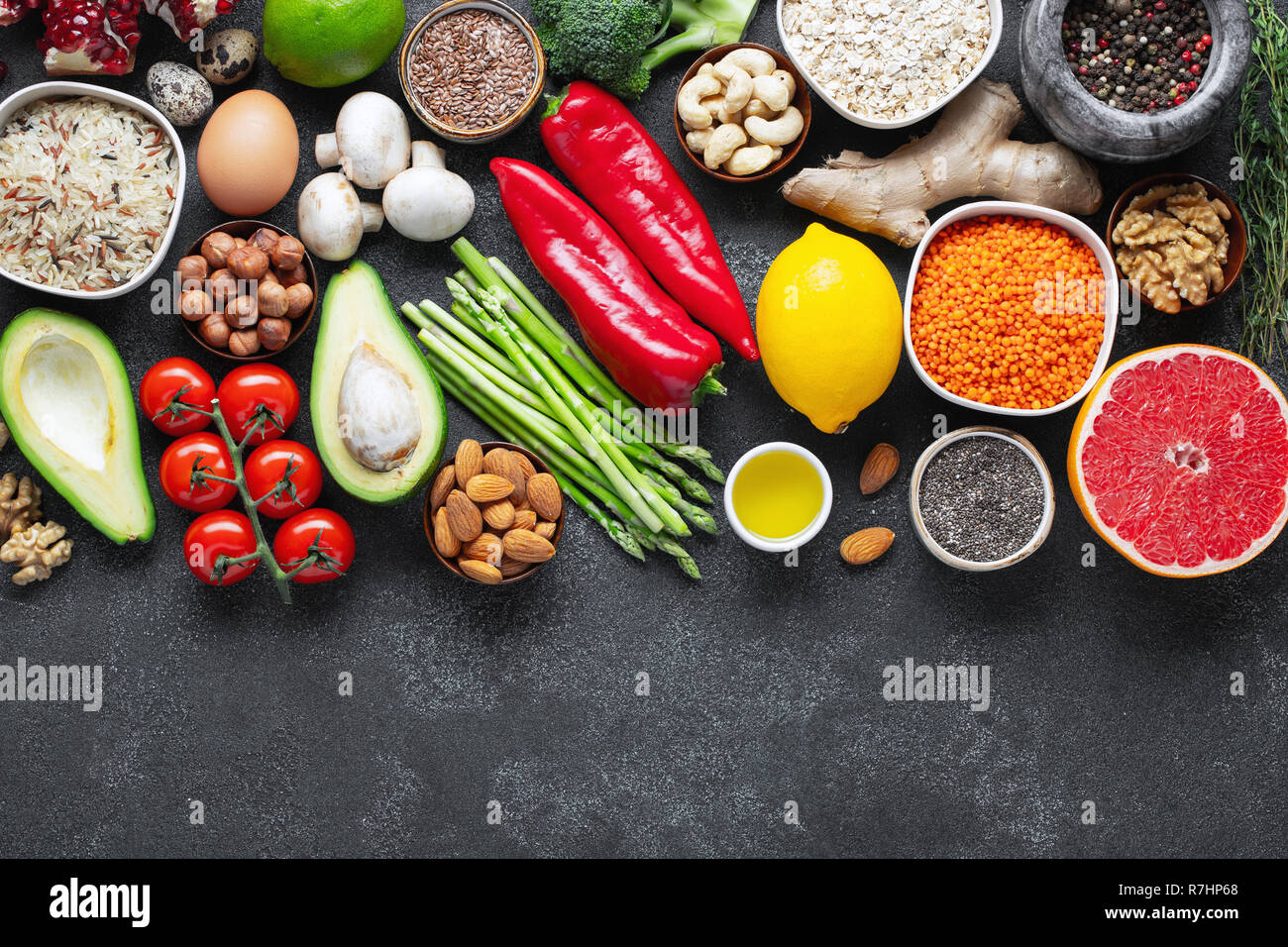 Healthy food clean eating selection: fruit, vegetable, seeds, superfood, cereal, leaf vegetable on black concrete background. Flat lay. Stock Photo
