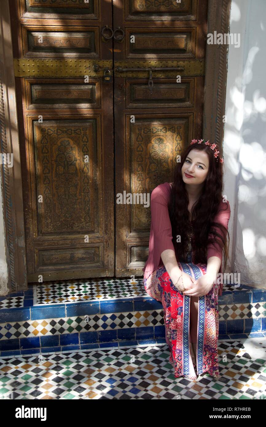 A hippie girl wearing pink clothes and hair flowers sits in a Moroccan doorway Stock Photo