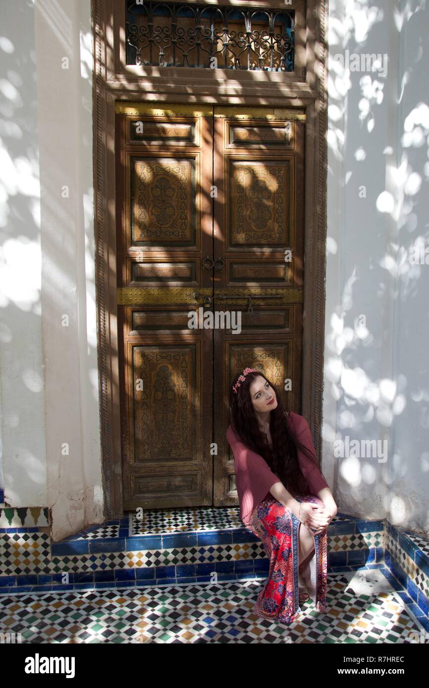 A hippie girl sits in a doorway in dappled sunlight Stock Photo