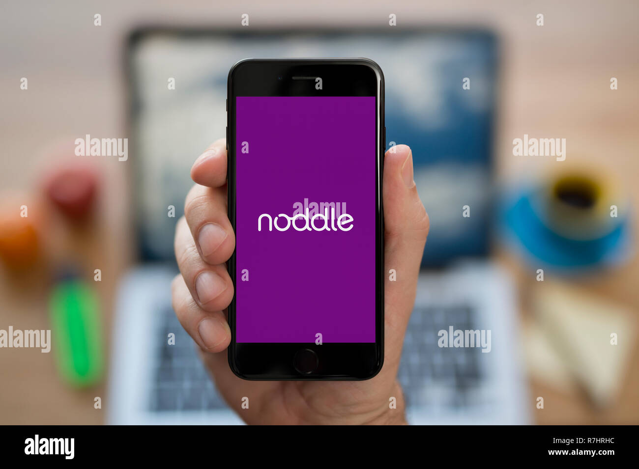 A man looks at his iPhone which displays the Noddle logo (Editorial use only). Stock Photo