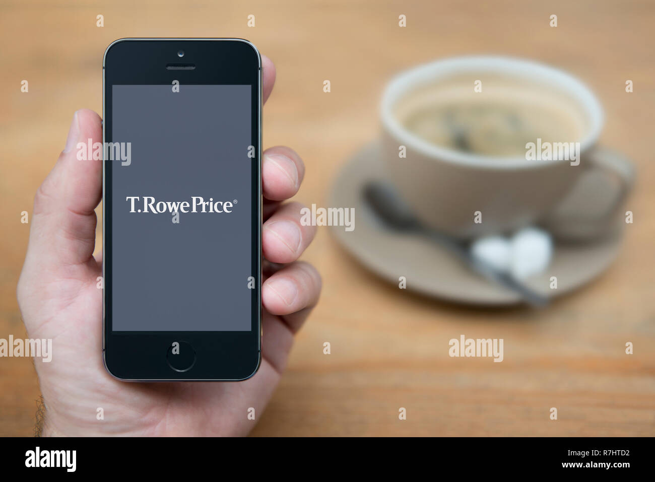 A man looks at his iPhone which displays the T.Rowe Price logo (Editorial use only). Stock Photo