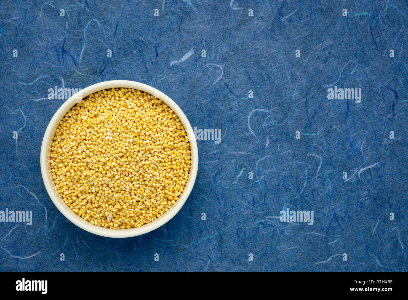 gluten free hulled millet grain in a ceramic bowl against blue mulberry