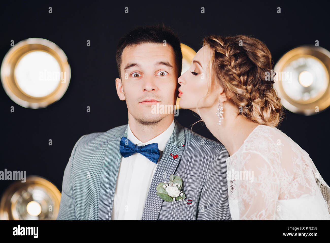 Funny Bridegroom With Eyes Open Wide Is Being Kissed By His