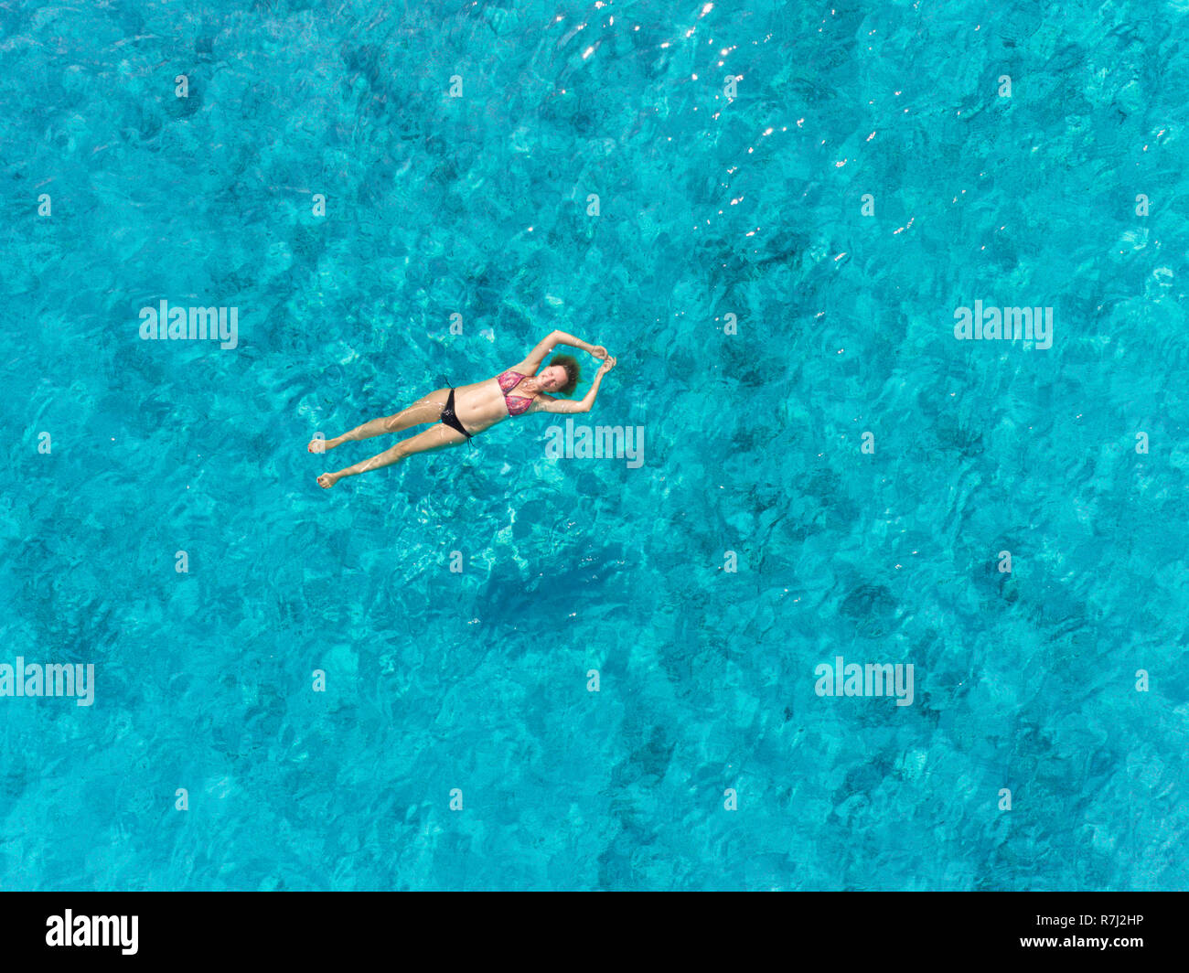 Aerial view of pregnant woman floating on her back in transparent sea with her arms above head. Stock Photo