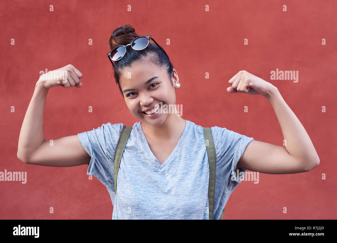 Smiling young Asian woman humorously flexing her arms outside Stock Photo