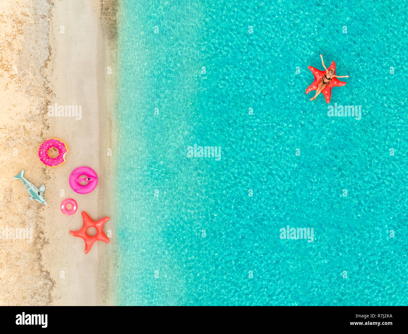 Aerial view of woman floating on inflatable star fish mattress by sandy beach and inflatable rings. Stock Photo