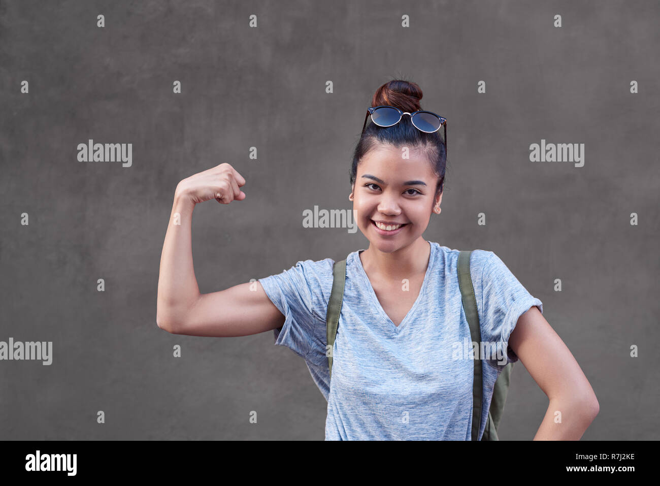 Joyful Asian woman smiling while flexing her bicep outside Stock Photo