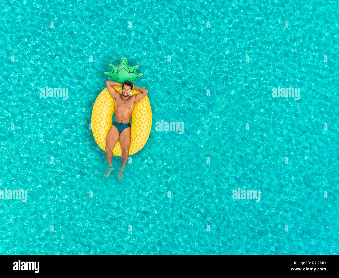 Aerial view of man floating on inflatable pineapple shaped mattress, smiling. Stock Photo