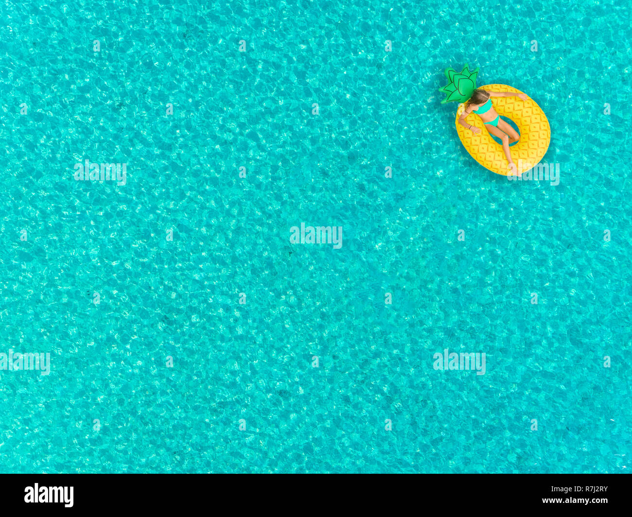 Aerial view of girl floating on inflatable pineapple mattress on transparent sea. Stock Photo