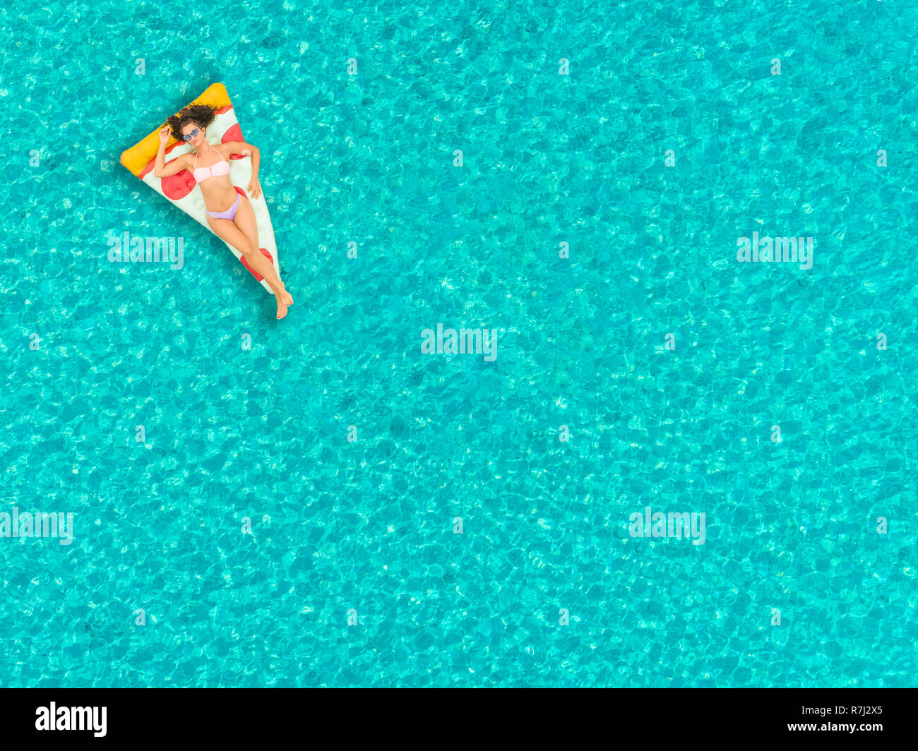 Aerial view of woman floating on inflatable pizza mattress, relaxing and smiling. Stock Photo