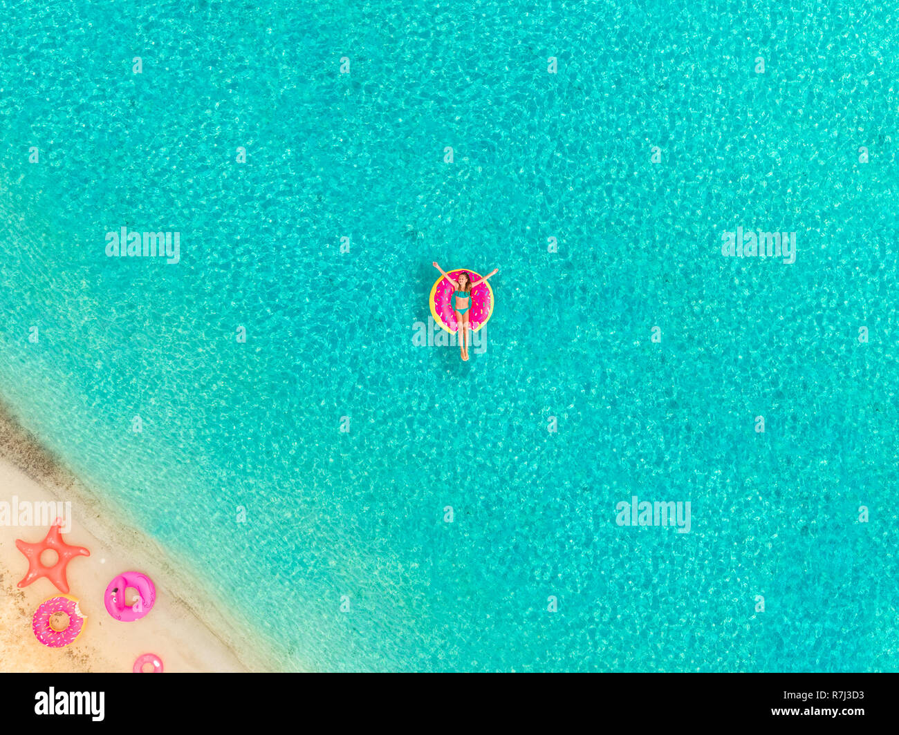 Aerial view of girl floating on inflatable donut mattress by sandy beach and inflatable rings. Stock Photo